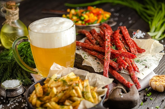 fleischsnacks für bier, neben einem glas bier, pommes frites in einer pfanne, auf einem rustikalen holztisch