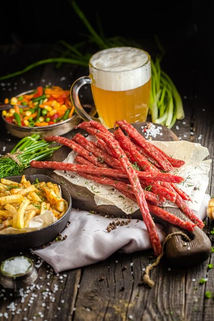 fleischsnacks für bier, neben einem glas bier, pommes frites in einer pfanne, auf einem rustikalen holztisch