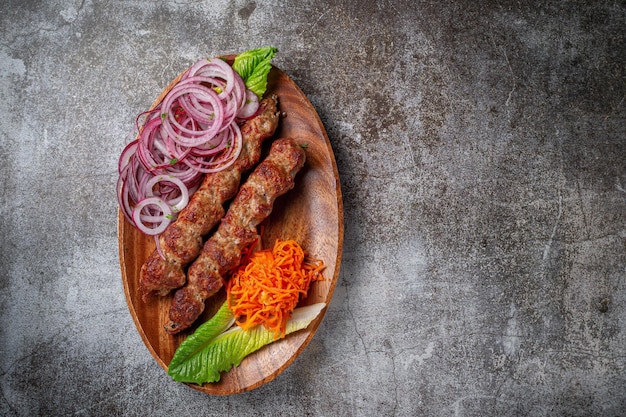 Fleischspieß und Grill mit Zwiebeln, koreanischen Karotten und grünem Salat in einem Teller vor dem Hintergrund eines grauen Steintisches