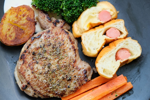 Fleischsteak mit dem gegrillten Gemüse und Gewürzen gelegt in eine Platte auf einen Holztisch