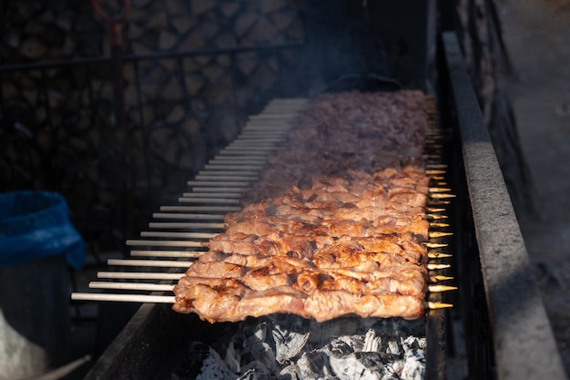 Fleischstücke, die bei Sonnenuntergang auf Metallspießen auf dem Grill aufgehängt werden