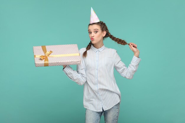 Flertando uma adolescente encantada em um cone de festa segurando seu presente de aniversário mandando beijos no ar
