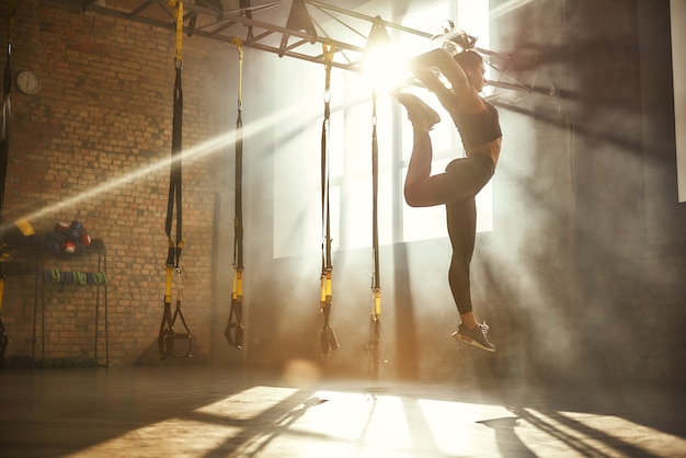 Flexibilidad perfecta de longitud completa de mujer atlética en ropa deportiva negra saltando mientras hace ejercicio
