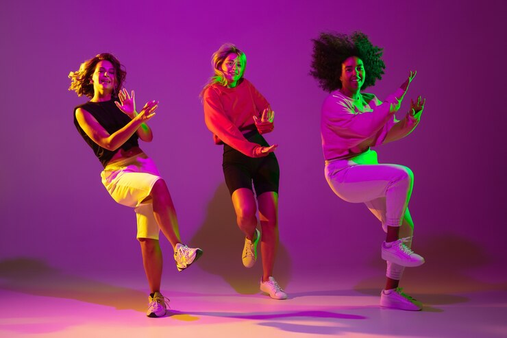 Foto flexible. chicas deportivas bailando hip-hop con ropa elegante sobre fondo rosa púrpura en el salón de baile con luz de neón verde. cultura juvenil, movimiento, estilo y moda, acción. retrato de moda.