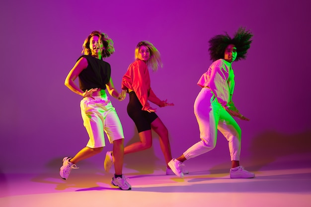 Foto flexível. meninas esportivas dançando hip-hop em roupas elegantes em fundo rosa-púrpura no salão de dança em luz de néon verde. cultura jovem, movimento, estilo e moda, ação. retrato elegante.