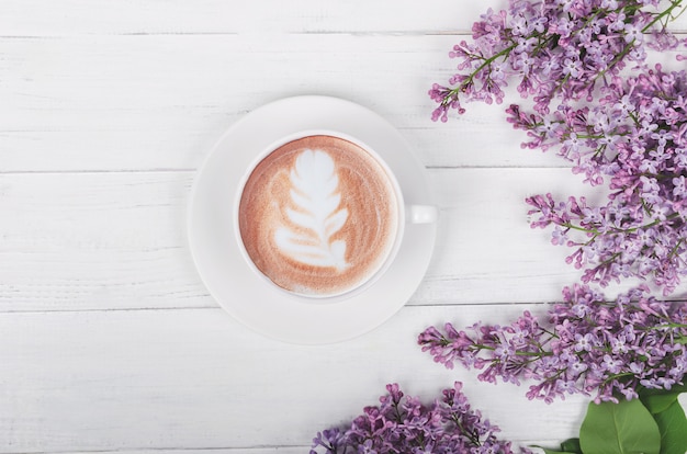 Flieder, Kaffee mit Latte Art auf hellem Holztisch. Romantischer Morgen. Flach lag