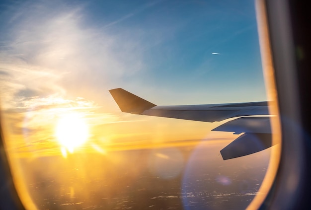 Fliegen und Reisen, Blick aus dem Flugzeugfenster auf den Flügel bei Sonnenuntergang. Flugzeugflügel unter Erde und Wolken. Reisen, Tourismus, Urlaub, Wochenende, Freiheit, Frieden, Hoffnungskonzepte