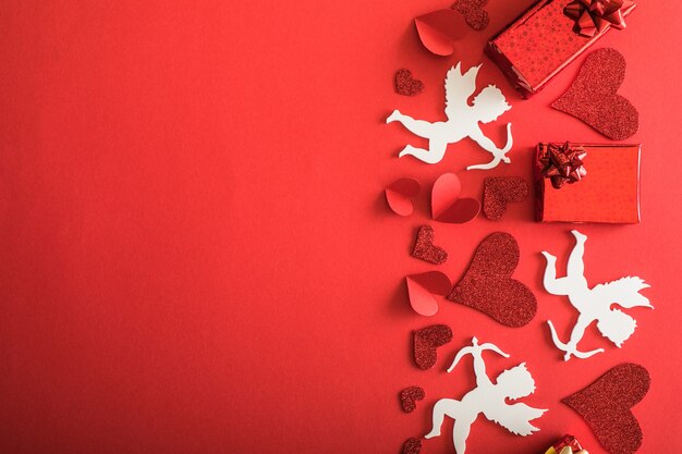 Fliegende Amor-Silhouette mit Herzen, Geschenken, glücklichen Valentinstag-Fahnen, Papierkunstart. Amour auf rotem Papier