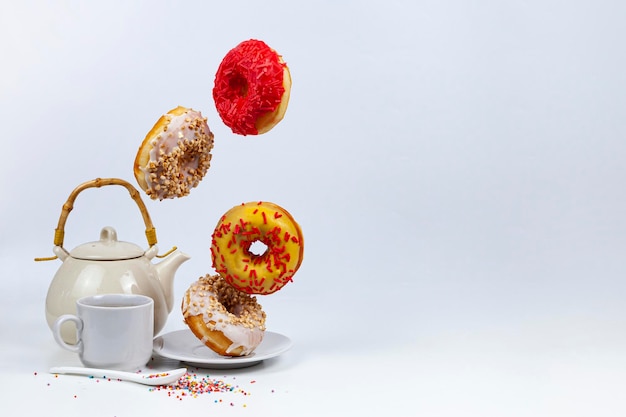 Fliegende Donuts und Tee auf weißem Hintergrund. Leckeres Frühstück.