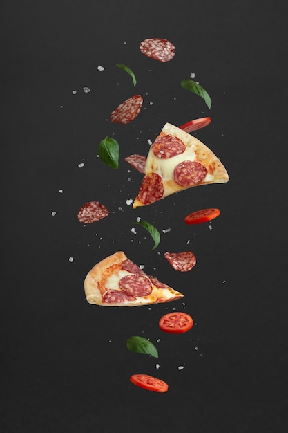 Fliegende Pizzenstücke und Zutaten auf schwarzem Hintergrund