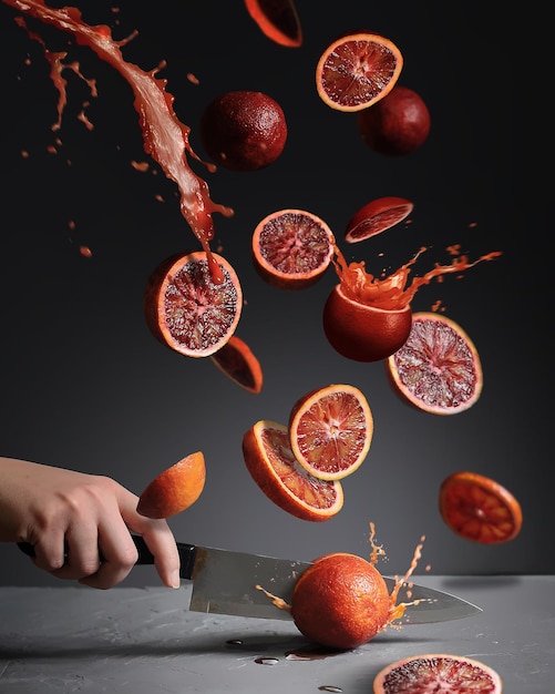 fliegende Scheiben roter Orangen mit Saftspritzern auf grauem Hintergrund Food Levitation Konzept