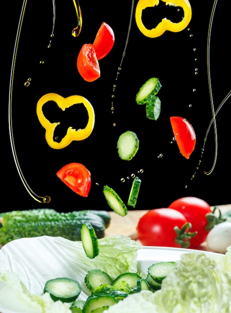 Fliegende Zutaten Salat isoliert auf einem schwarzen. Salat schwimmt in der Luft über dem Tisch. Salatgemüse und Olivenöl