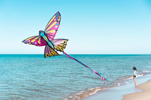 Fliegender Drachen am Strand, während das kleine Mädchen allein an der Küste spielt Konzept der Kindheit und Einsamkeit