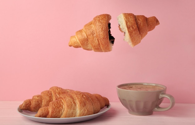 Fliegendes Croissant mit Kaffee auf rosa Hintergrund