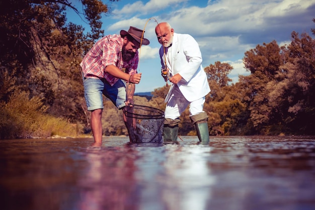 Fliegenfischer am Fluss Fliegenfischen ist am bekanntesten als Methode zum Fangen von Forellen, Äschen und Lachsen Porträt von zwei fröhlichen bärtigen Männern beim Fischen