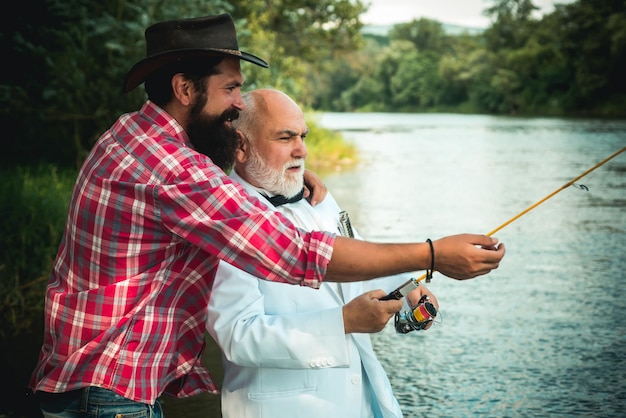 Fliegenrute und Rolle mit einer Bachforelle aus einem Bach Vater und Sohn entspannen sich zusammen Männer, die während des Sommertages im Fluss fischen Mann, Fischen