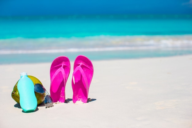 Flip Flops, Kokos und Sonnencreme auf weißem Sand. Strandzubehör.