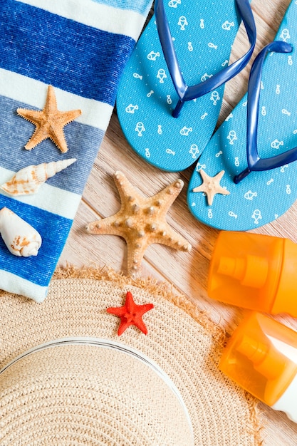 Flip-Flops, Strohhut, Seestern, Sonnencreme-Flasche, Bodylotion-Spray auf Holzhintergrund-Draufsicht. flach legen Sommer Strand Meer Zubehör Hintergrund, Reisekonzept.