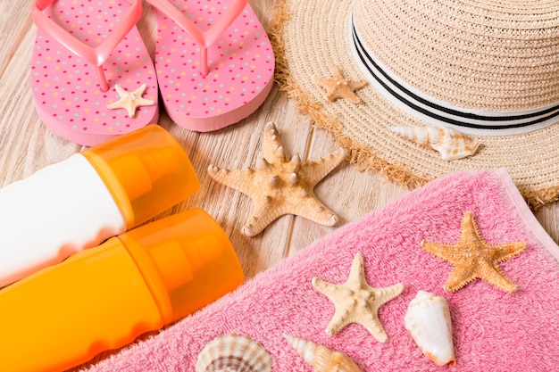 Flip-Flops, Strohhut, Seestern, Sonnencreme-Flasche, Bodylotion-Spray auf Holzhintergrund-Draufsicht. flach legen Sommer Strand Meer Zubehör Hintergrund, Urlaubskonzept.