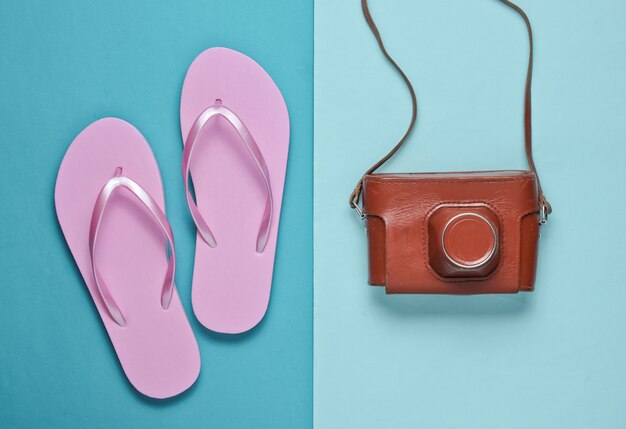 Flip Flops und Retro-Kamera auf blauem Papierhintergrund. Reise, Urlaubskonzept. Sommermode, Urlaub. Strandzubehör.