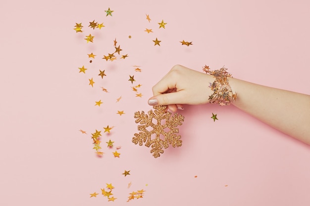 Foto floco de neve dourado em mão feminina e estrelas douradas em fundo rosa conceito de férias de natal megical