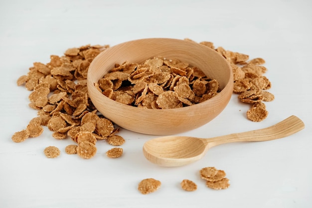 Flocos de cereais secos e crocantes em uma tigela de madeira com colher de pau no fundo branco