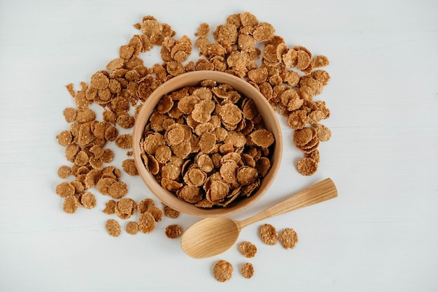 Flocos de cereais secos e crocantes em uma tigela de madeira com colher de pau no fundo branco