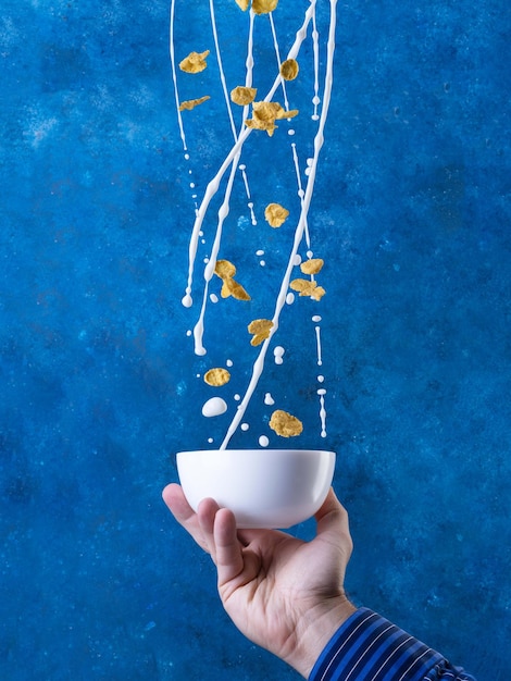 Flocos De Milho Com Respingo De Leite. Café da manhã saudável. Levitação sobre fundo azul.