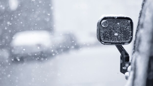 Flocos de neve caem em um espelho de carro em uma rua da cidade de inverno. Queda de neve ou nevasca.