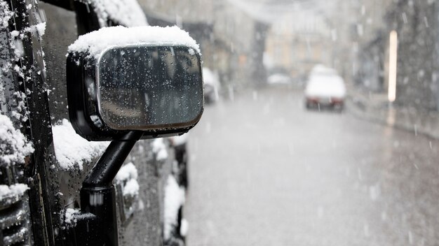 Flocos de neve caem em um espelho de carro em uma rua da cidade de inverno. Queda de neve ou nevasca.