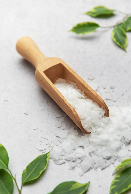 Flocos de magnesio que se derraman de una cuchara de madera sobre una superficie de mármol con hojas verdes