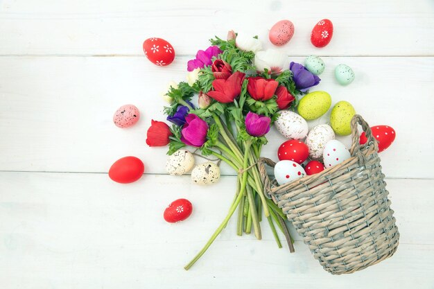 Flor de amapola y huevos de Pascua en una mesa de madera blanca de cesta de mimbre