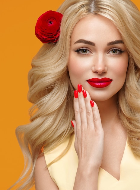 Flor de cabello rubio largo y rizado de mujer de belleza en uñas cuidadas de cabello. Colores de moda naranja y amarillo.