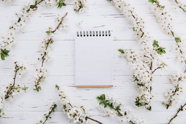 Flor de cerezo y cuaderno vacío en mesa de madera blanca