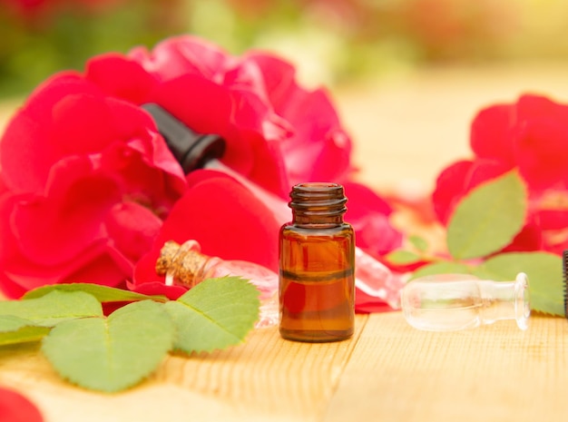 Flor de rosa rosa e copo de óleo essencial engarrafado ou água de rosas com pétalas de rosa no conceito de aromaterapia de mesa de madeira