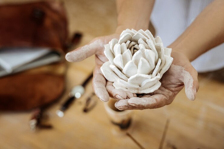 Foto flor decorativa. hombre práctico haciendo hermosa flor decorativa de cerámica mientras trabajaba en su taller