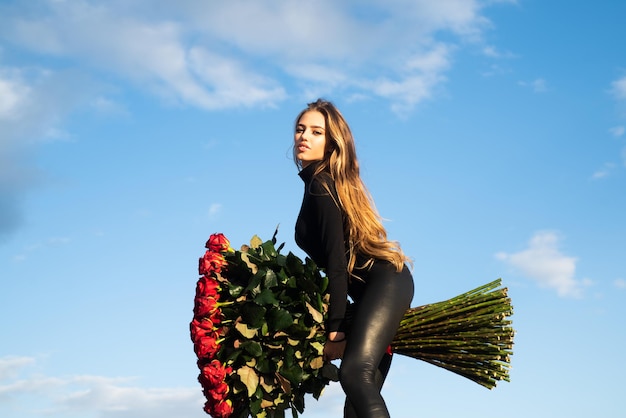 Flor do amor. Mulher com buquê de rosas ao ar livre. Presente de dia dos namorados. Linda garota no fundo do céu. Senhora e rosas. Flores favoritas.