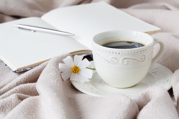 Flor en el libro y la taza de café negro frente a la ventana en la mañana