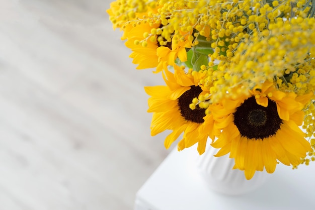 Flor de Mimosa y girasoles en jarrón de cerámica blanca sobre fondo de pared de ladrillo blanco con espacio para texto