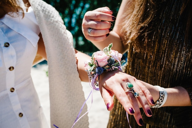 Flor na lapela decorada à mão com flores e fitas A namorada da noiva tem em mãos Casas de botão Estilo de festa boho Noite de solteira Festas de despedida de solteiro Fechar o fundo da praia natureza