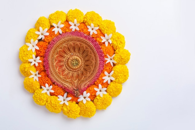 Flor Rangoli para Diwali Festival hecha con caléndula y hojas y lámpara de aceite sobre fondo blanco.