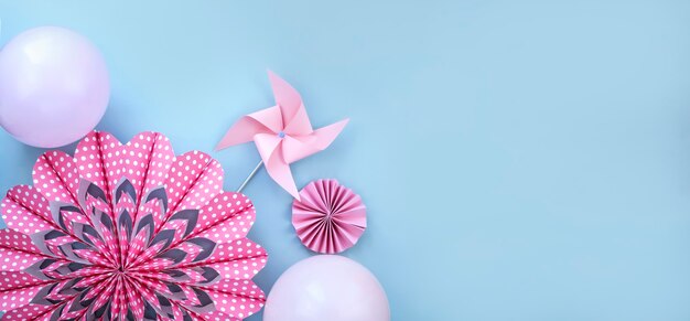 Flor rosa feita de papel moinho de vento e balões na parede azul clara