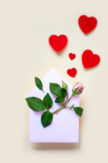Una flor rosa en miniatura con hojas y corazones se encuentra en un sobre. Sobre un fondo claro. Concepto de San Valentín