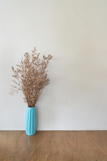 Foto flor seca em vaso turquesa em mesa de madeira sobre parede bege