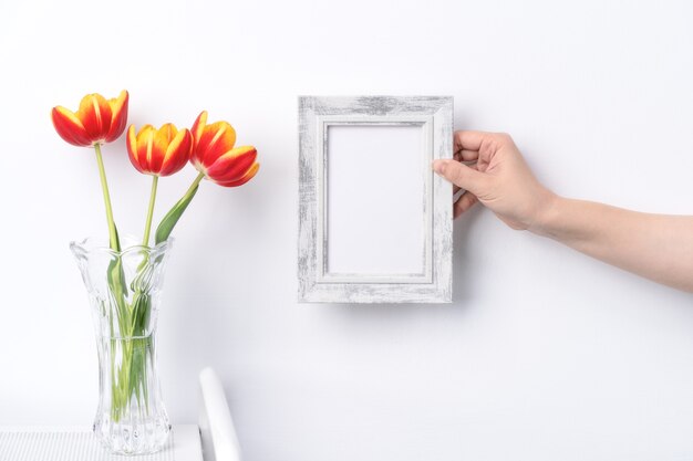 Flor de tulipán en florero de vidrio con lugar de marco de imagen sobre fondo de mesa de madera blanca contra una pared limpia en casa, de cerca, concepto de decoración del día de la madre.