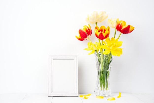 Flor de tulipán en jarrón de vidrio con marco de imagen en el fondo de la mesa de madera blanca contra la pared limpia en casa cerca del concepto de decoración del Día de la Madre