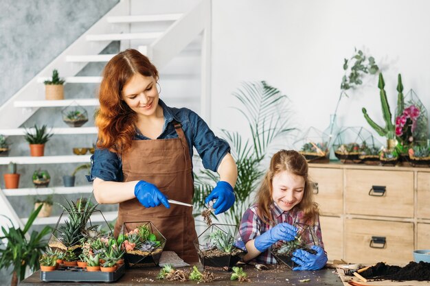 Florario de bricolaje. Jardinería doméstica. Madre e hija disfrutando de la plantación de suculentas, divirtiéndose, sonriendo.