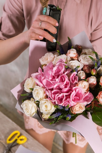 Floreria envolviendo ramo de flores color de rosa. El decorador trabaja en un invernadero con un ramo de rosas. Taller florístico, habilidad, decoración, concepto de pequeña empresa.