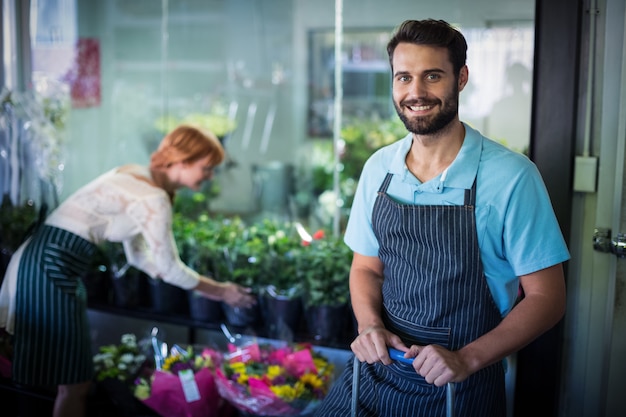 Floreria masculina de pie mientras que florista femenina trabajando en segundo plano