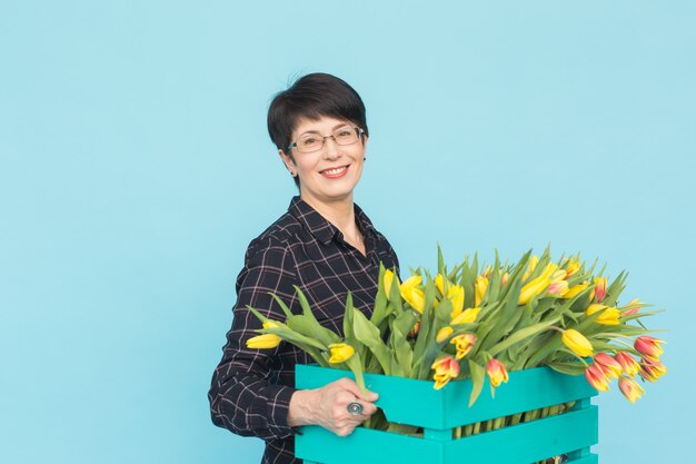 Floreria de mediana edad sosteniendo una caja de madera azul de tulipanes en estudio